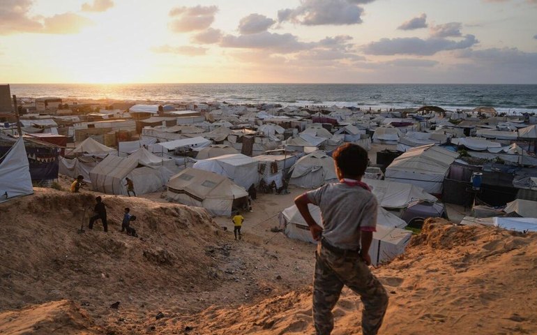 Palestinos deslocados caminham por um acampamento de tendas em Muwasi, uma área que Israel designou como zona segura
