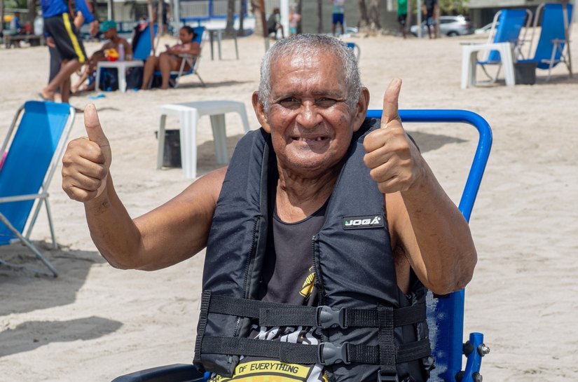 Cadeira anfíbia auxilia pessoa idosa a tomar banho de mar assistido