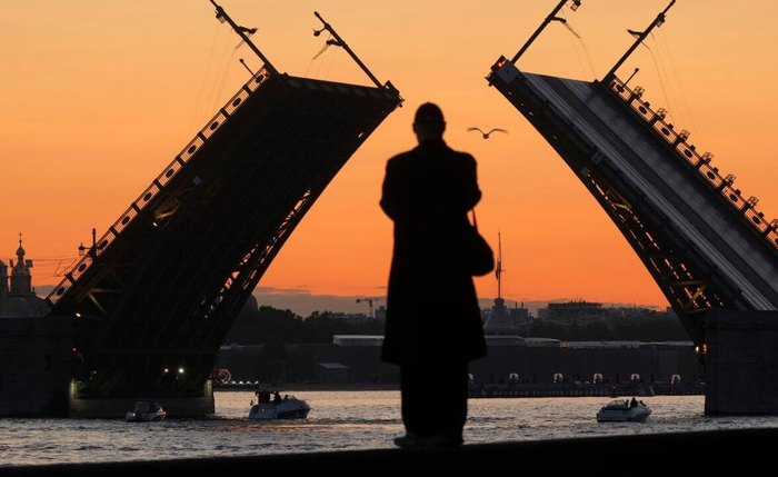 Homem olha para Ponte do Palácio no rio Neva ao nascer do sol