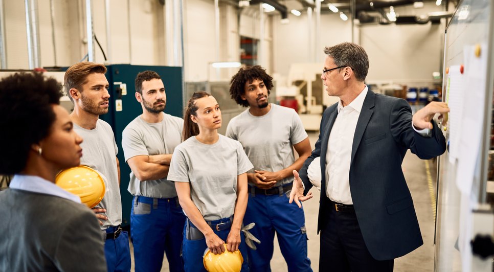 mid-adult-businessman-giving-presentation-to-group-of-industrial-workers-in-a-factory / Foto: <a href='https://br.freepik.com/fotos-vetores-gratis/lideranca'>Liderança foto criado por Drazen Zigic - br.freepik.com</a>
