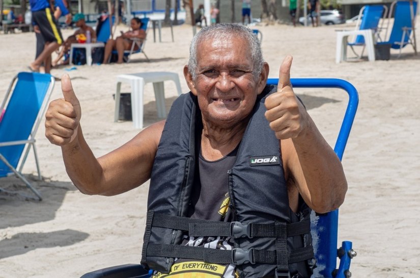 Cadeira anfíbia auxilia pessoa idosa a tomar banho de mar assistido